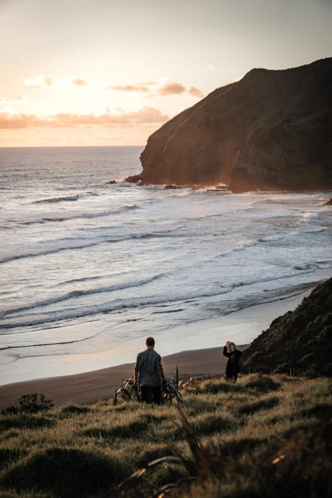 Tranquil New Zealand beach scene at sunset with two people enjoying the view.